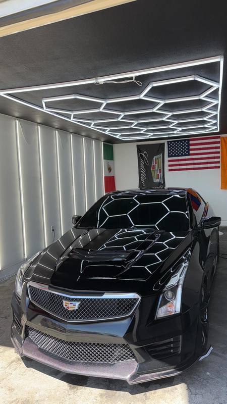 Cadillac ATS-V with its windows freshly tinted, shot head-on under the hexagon LED array so the array reflects whole across the gloss black hood and the darkened glass reads evenly dark corner to corner