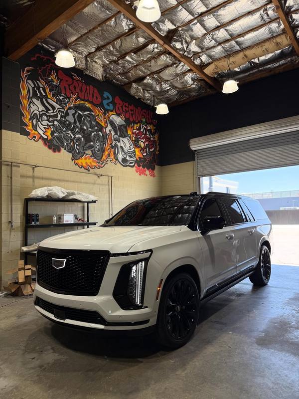 Cadillac Escalade after a Peel Clear color change to satin grey, with the hood, doors and tailgate in the new flat grey and the roof, pillars, grille and wheels left gloss black; parked inside the shop under the mural